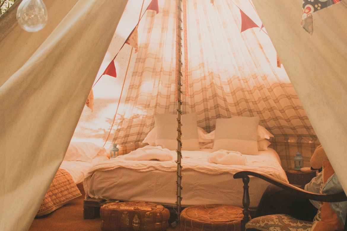 A softly lit sun soaked mage showing a double bed inside a glamping teepee